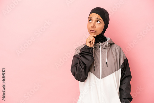 Young Arab woman with sport burqa isolated on pink background looking sideways with doubtful and skeptical expression.