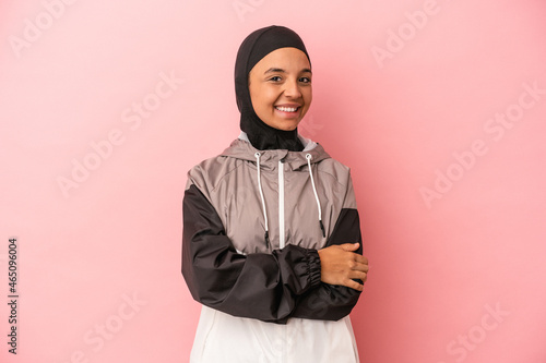 Young Arab woman with sport burqa isolated on pink background who feels confident, crossing arms with determination.