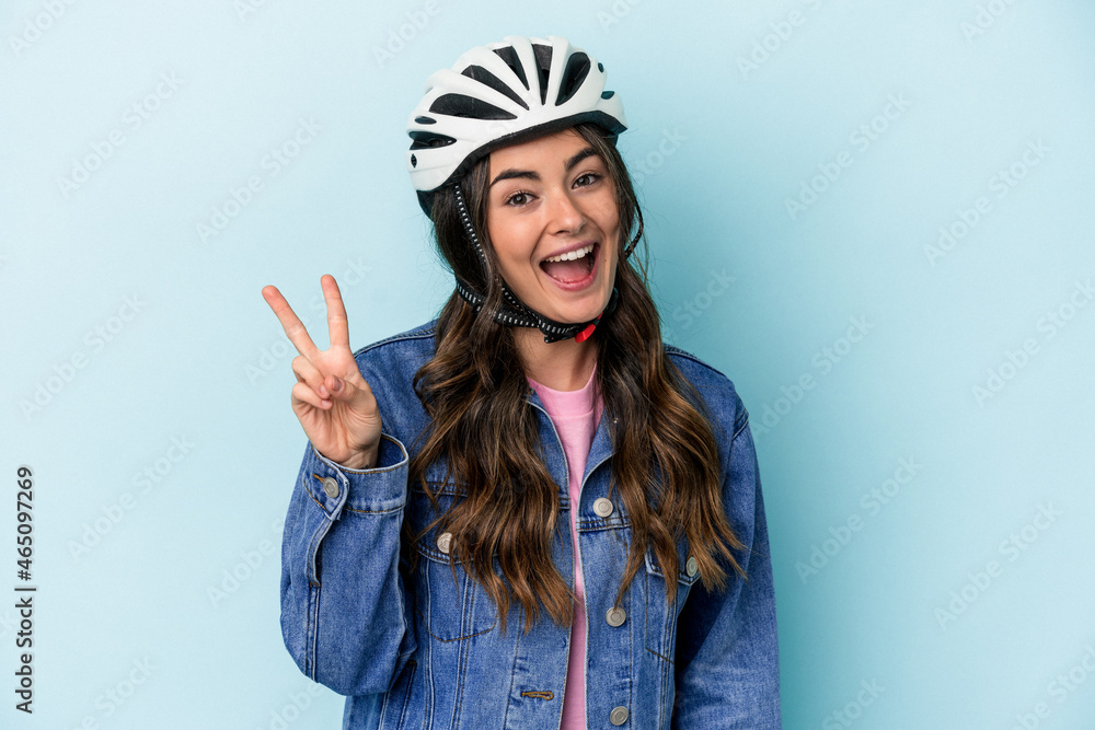 Young caucasian woman rinding a bike isolated on blue background joyful and carefree showing a peace symbol with fingers. Young caucasian woman rinding a bike isolated on blue background joyful and carefree showing a peace symbol with fingers.