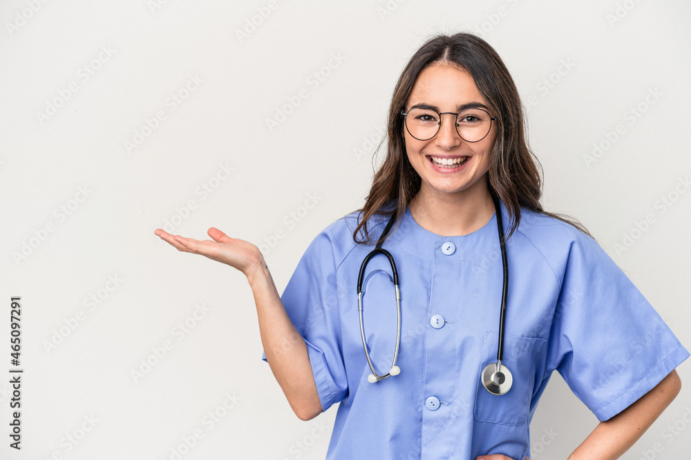 Young caucasian nurse woman isolated on white background showing a copy space on a palm and holding another hand on waist. Young caucasian nurse woman isolated on white background showing a copy space on a palm and holding another hand on waist.