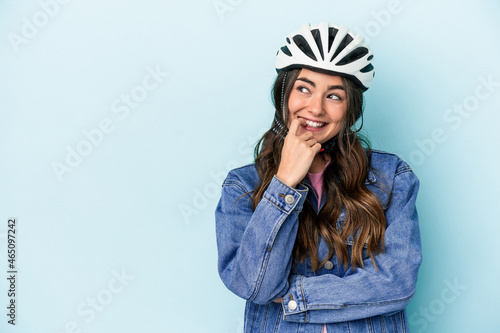 Young caucasian woman rinding a bike isolated on blue background relaxed thinking about something looking at a copy space. © Asier