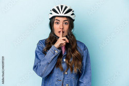 Young caucasian woman rinding a bike isolated on blue background keeping a secret or asking for silence. © Asier