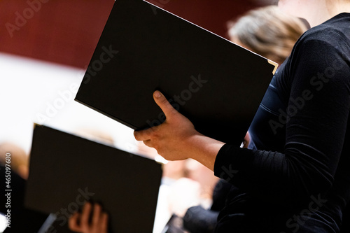 Canvas-taulu Singers of a choir dressed all in black singing in a concert from black folders