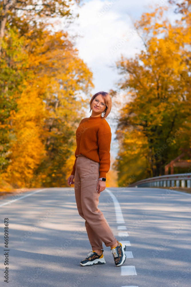 Fototapeta premium Smiling woman in a cozy sweater looks at the camera with her hands to the side an autumn forest