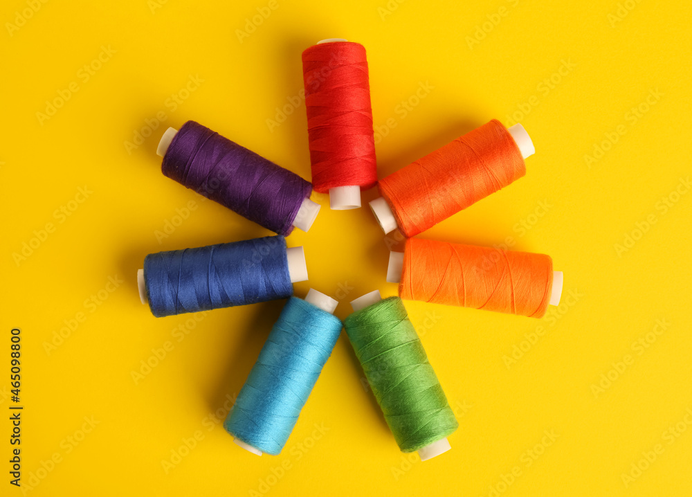 Different colorful sewing threads on yellow background, flat lay Different colorful sewing threads on yellow background, flat lay
