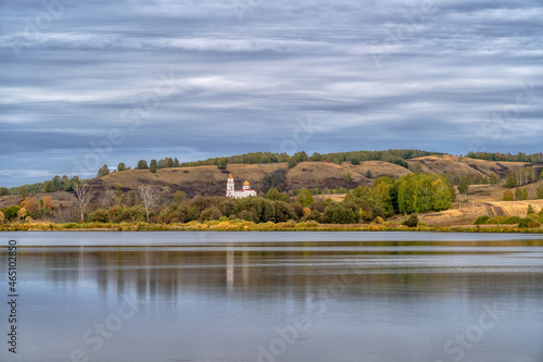 White temple in a hilly area on the shore of a reservoir. The sky is covered with clouds.