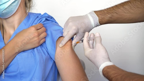 Nurse with white gloves administering the dose of the vaccine to achieve group immunization for the Covid-19 virus or coronavirus to the hospital health staff with a mask.	