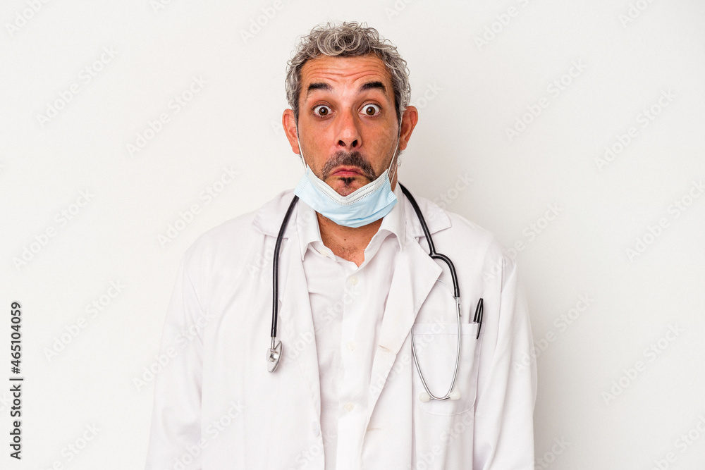 Middle age doctor man wearing a mask for virus isolated on white background shrugs shoulders and open eyes confused. Middle age doctor man wearing a mask for virus isolated on white background shrugs shoulders and open eyes confused.