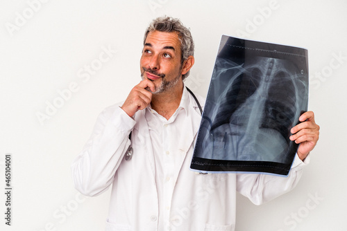 Middle age doctor caucasian man holding a radiography isolated on white background looking sideways with doubtful and skeptical expression.