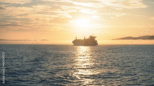 Freight cargo ship sails through the sea at sunset