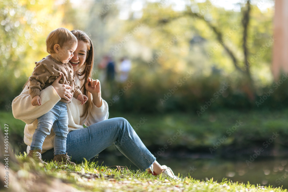Young mother with a one-year-old toddler walking and hugging in the autumn park Young mother with a one-year-old toddler walking and hugging in the autumn park