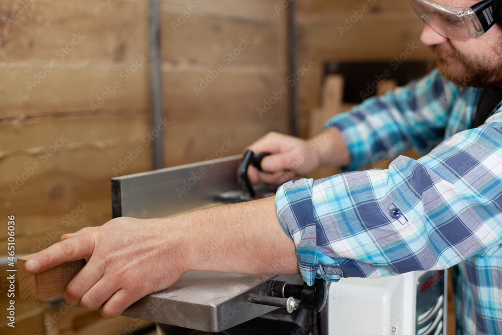  A carpenter in a plaid shirt works at a machine in a workshop. Wood. Ecological compatibility. Lifestyle. Close up