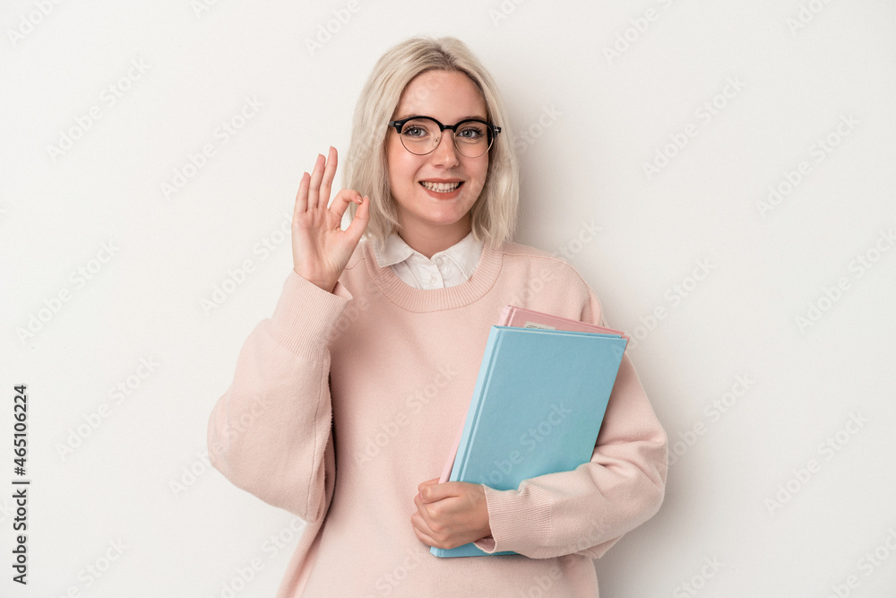 Young caucasian student woman holding books isolated on white background cheerful and confident showing ok gesture.