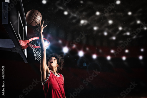 Basketball player in red uniform jumping high to make a slam dunk to the basket photo