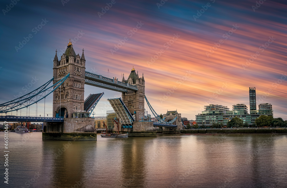 Long exposure view of the lifted Tower Bridge in London with a ship passing by during sunset time