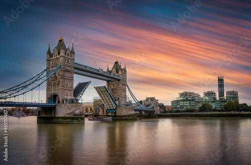 Long exposure view of the lifted Tower Bridge in London with a ship passing by during sunset time