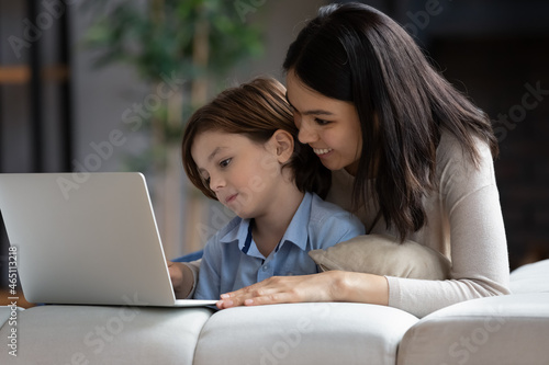 Happy millennial Asian mom and gen Z son boy watching movie, media content on laptop computer, using app, service, chatting online. Mother and son shopping, booking on internet at home © fizkes