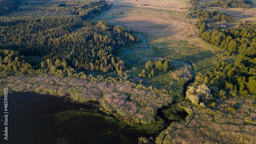 Aerial view of the lake and small curved river in a sunny day. Bird's eye view of the fields and green forest.