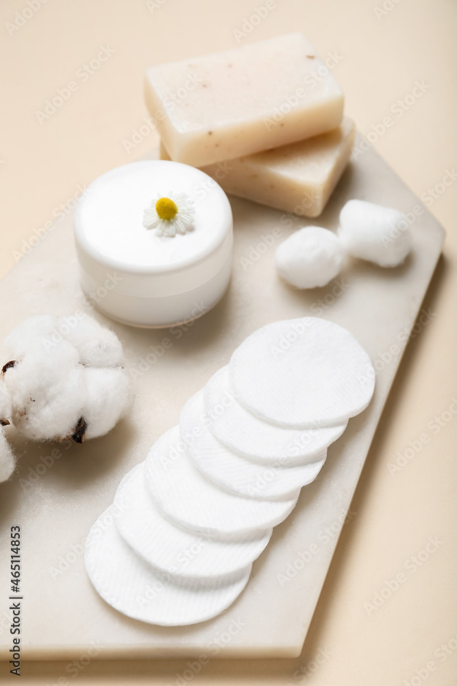 Board with cotton pads, flowers and cosmetic products on color background Board with cotton pads, flowers and cosmetic products on color background