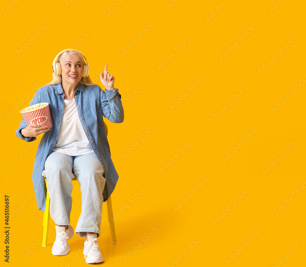 Fototapeta premium Mature woman with tasty popcorn pointing at something on color background