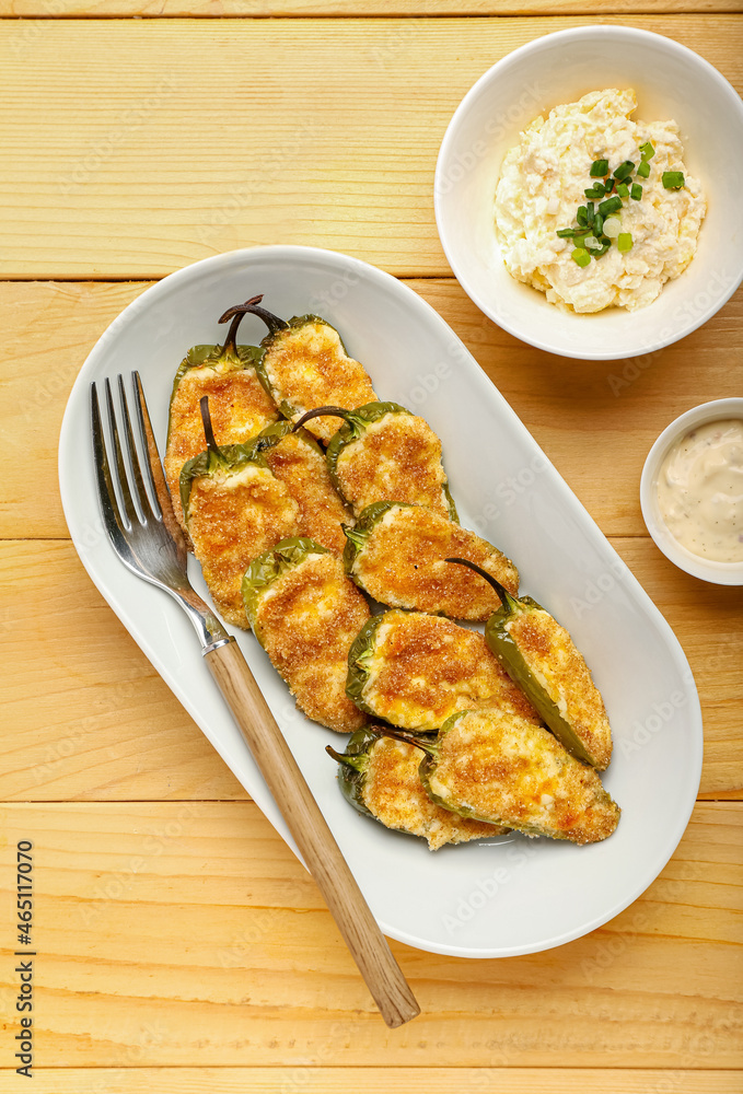 Plate with delicious jalapeno poppers and sauce on wooden background Plate with delicious jalapeno poppers and sauce on wooden background