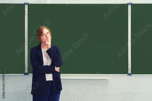 A school teacher stands doubtfully in front of an empty blackboard, copy space for the inscription. Problems with learning via the Internet during the flu virus epidemic photo