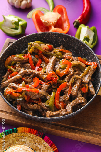 Frying pan with tasty beef Fajita and sombrero hat on color background