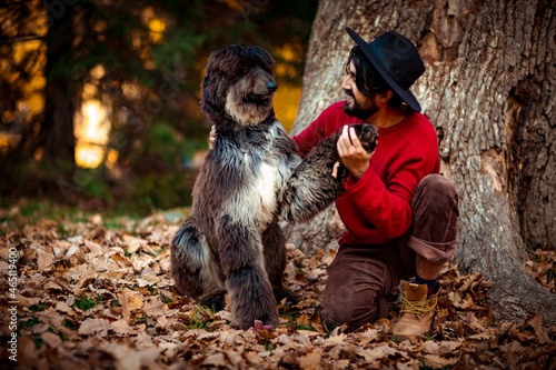 a young man, dark-haired, in a red sweater and hat,sitting under a tree with a pet dog,in the afternoon in the autumn park