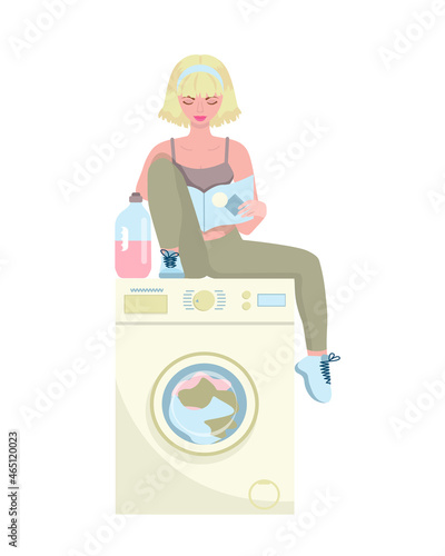 Happy woman sitting in the laundry room on the washing machine and reading a book