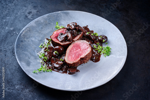 Modern style traditional fried dry aged angus beef filet medaillons natural with mushrooms in red wine sauce served as close-up on a design plate with copy space