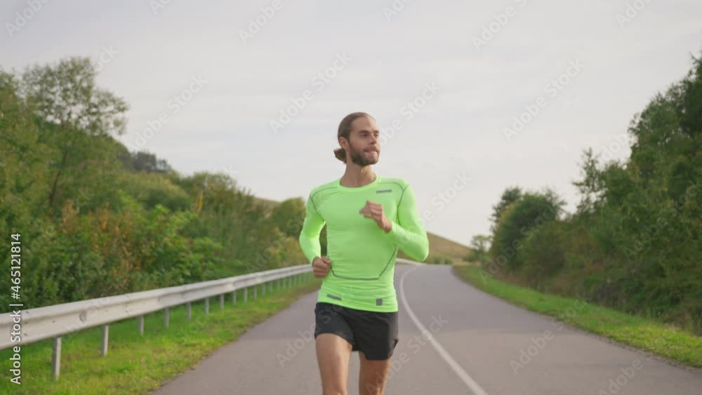 Confident male runner jogging on the empty road in cloudy morning. Athletic active young bearded sportsman running outside. Country highway. People, recreation and sports. Confident male runner jogging on the empty road in cloudy morning. Athletic active young bearded sportsman running outside. Country highway. People, recreation and sports.