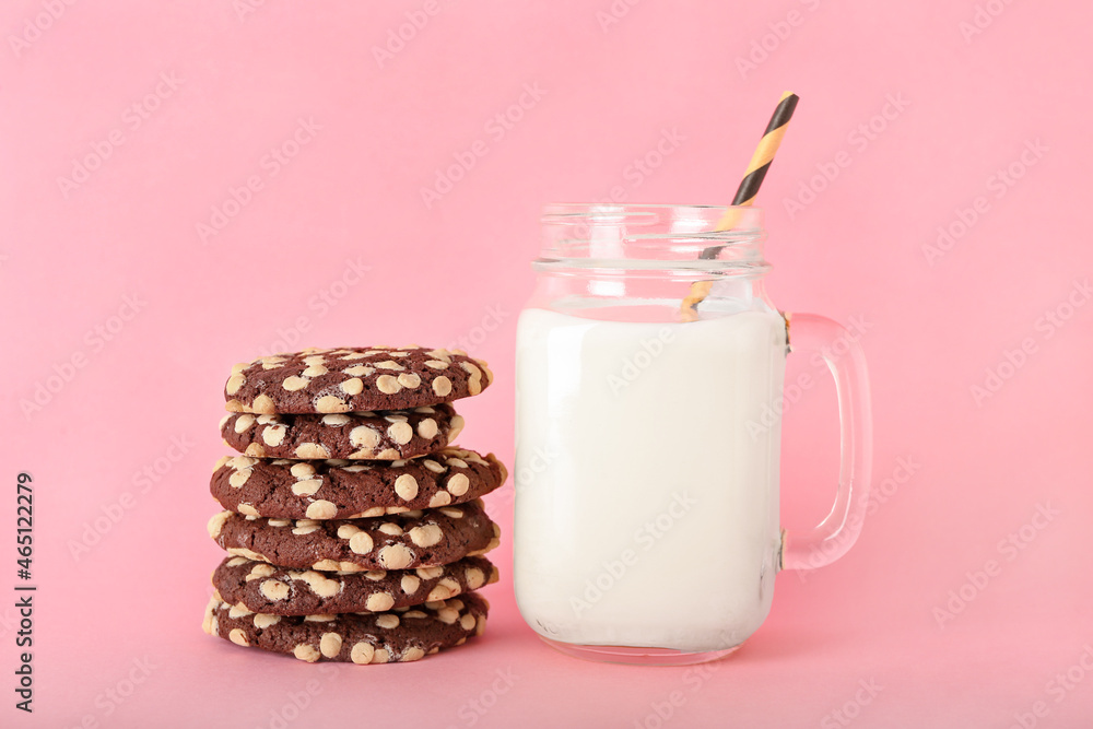 Tasty cookies with white chocolate chips and mason jar of milk on color background Tasty cookies with white chocolate chips and mason jar of milk on color background