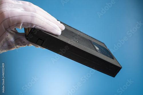 Hand holds retro HVS video cassette on a blue background. Retro wave. 80s 90s. Open film.
