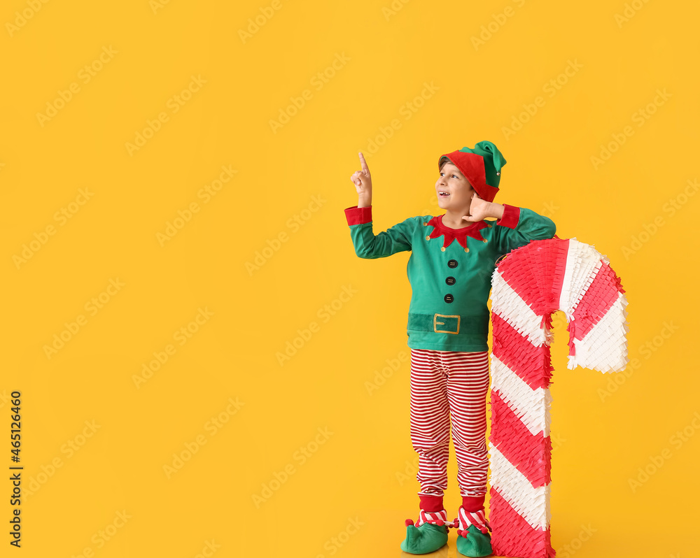 Cute little boy dressed as elf with candy cane pinata pointing at something on color background Cute little boy dressed as elf with candy cane pinata pointing at something on color background