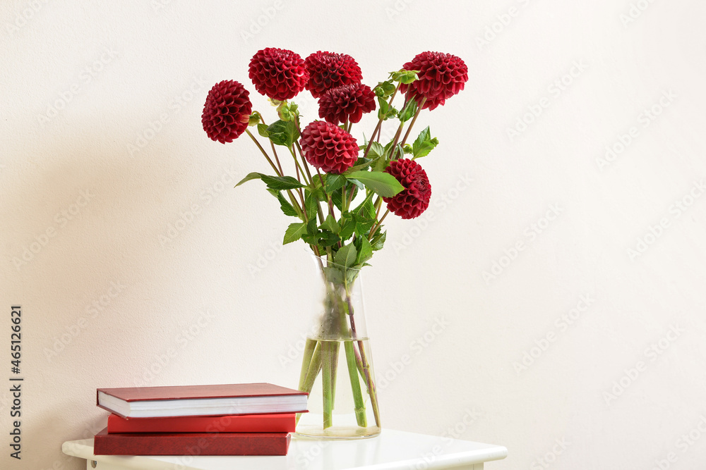 Vase with dahlias and notebooks on table against color background Vase with dahlias and notebooks on table against color background