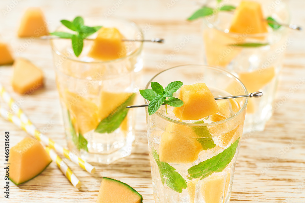 Fototapeta premium Melon lemonade with ice and mint in a glass on a wooden table. Melon drink in glasses with melon slices. melon water in glass jars.