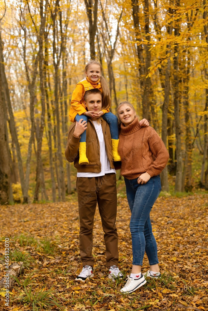 a young handsome guy in an autumn beige jacket is holding a little girl in a yellow raincoat next to his young mother in a brown knitted sweater autumn city park forest a young handsome guy in an autumn beige jacket is holding a little girl in a yellow raincoat next to his young mother in a brown knitted sweater autumn city park forest