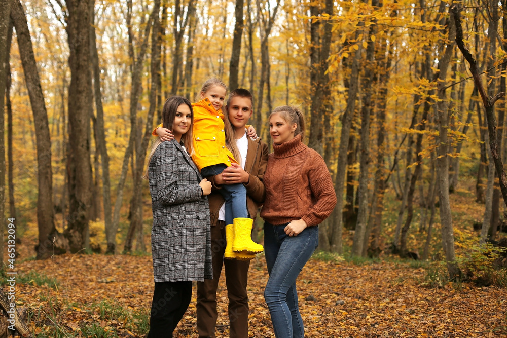 a young handsome guy in an autumn beige jacket is holding a little girl in a yellow raincoat next to young beautiful girls are standing autumn city forest park a young handsome guy in an autumn beige jacket is holding a little girl in a yellow raincoat next to young beautiful girls are standing autumn city forest park