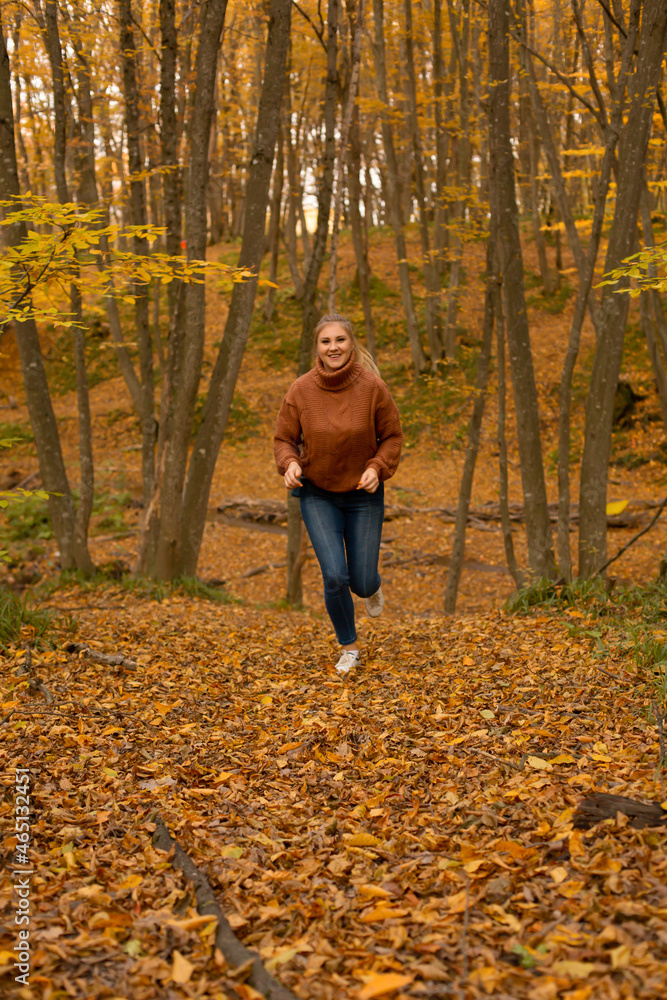 a young blonde girl in a brown knitted sweater in jeans runs in the autumn forest healthy lifestyle