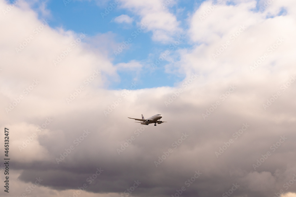 A passenger plane with a light beacon at the bottom of the fuselage on the background of cloudy sky on a cloudy day A passenger plane with a light beacon at the bottom of the fuselage on the background of cloudy sky on a cloudy day