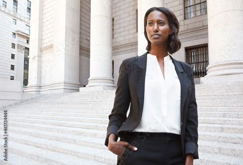 A female lawyer (or business person) stands in front of a courthouse or municipal building in thought. photo