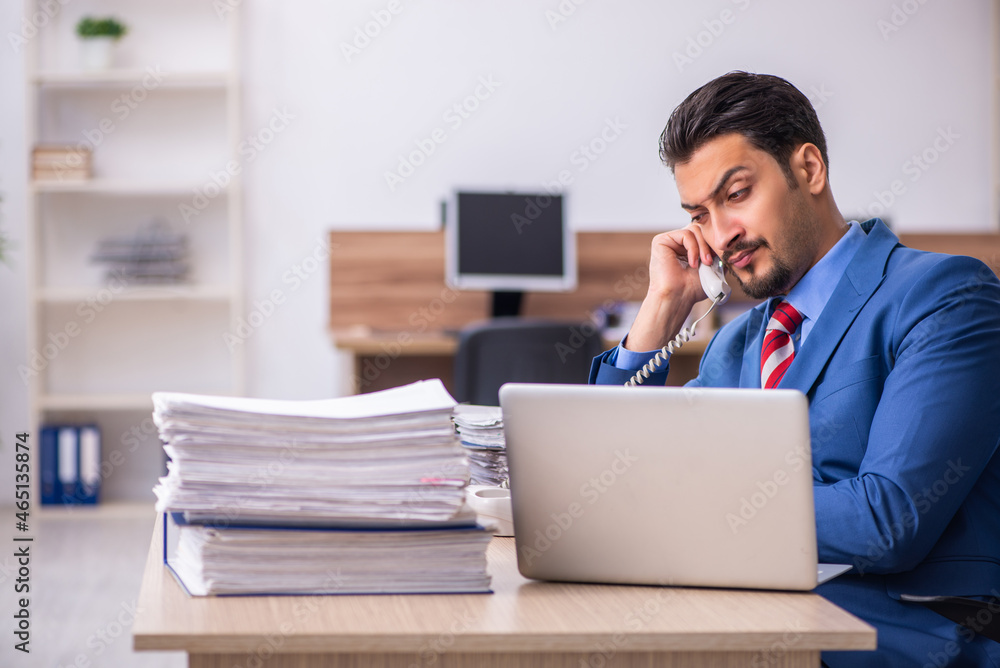 Young male employee unhappy with excessive work at workplace Young male employee unhappy with excessive work at workplace