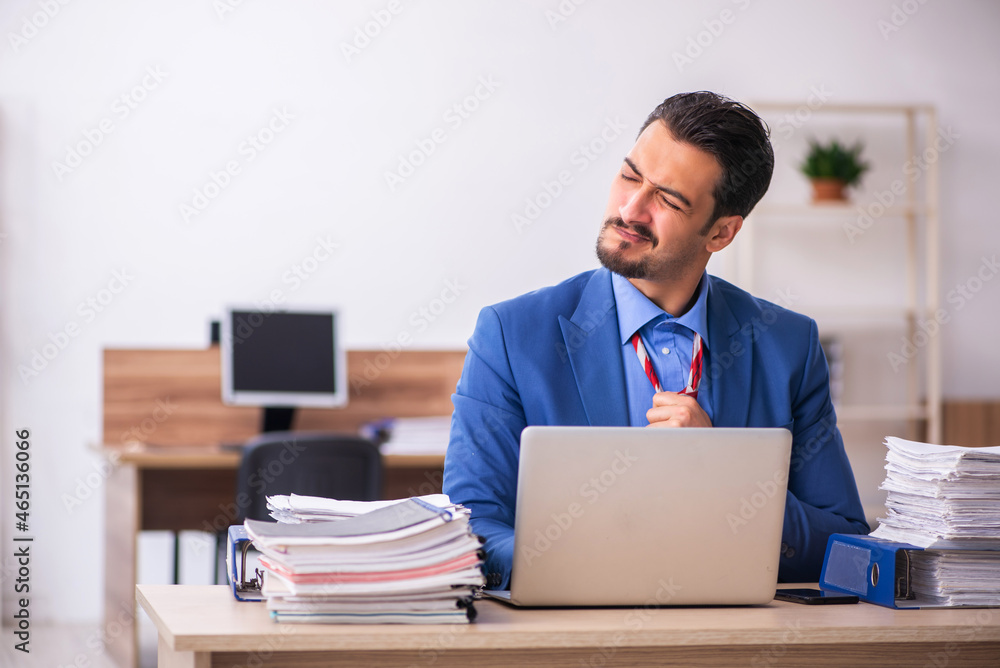 Young male employee unhappy with excessive work at workplace Young male employee unhappy with excessive work at workplace