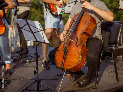 Male cellist playing violoncello in orchestra outdoors