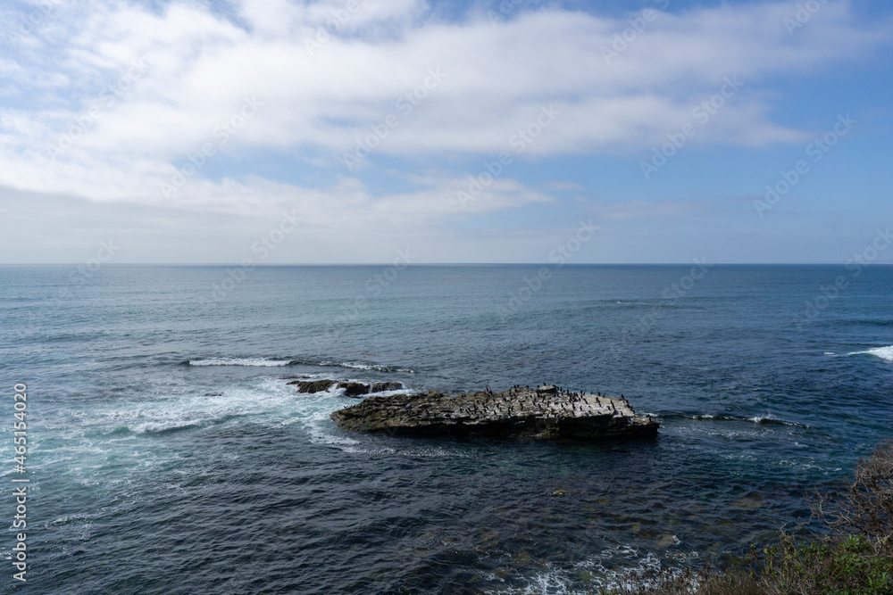 A view of Pacific Ocean and a rocky little island with colony of sea birds on it