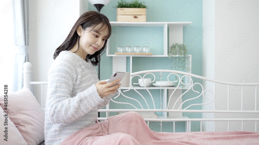 ベッドでスマートフォンを使う女性 ベッドでスマートフォンを使う女性