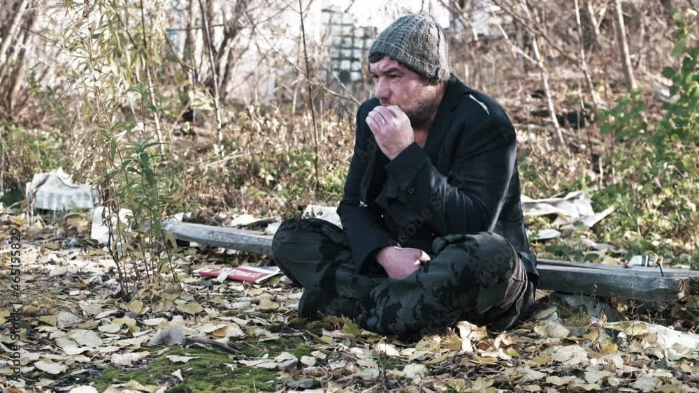 a hungry homeless unshaven man on the street in a torn suit smokes a cigarette an old beggar wants to eat a refugee without documents is sitting on the ground.. a hungry homeless unshaven man on the street in a torn suit smokes a cigarette an old beggar wants to eat a refugee without documents is sitting on the ground..