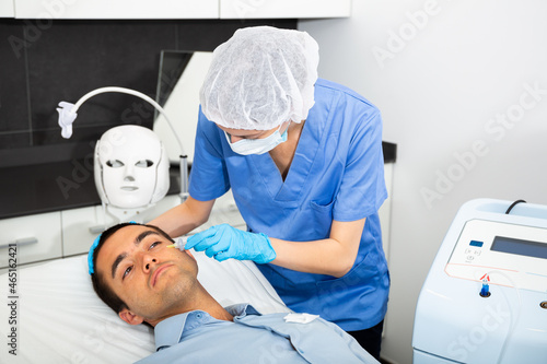 Female cosmetologist injecting carbon dioxide under face skin of male client to increase blood flow in capillaries and rejuvenate skin. Carboxytherapy