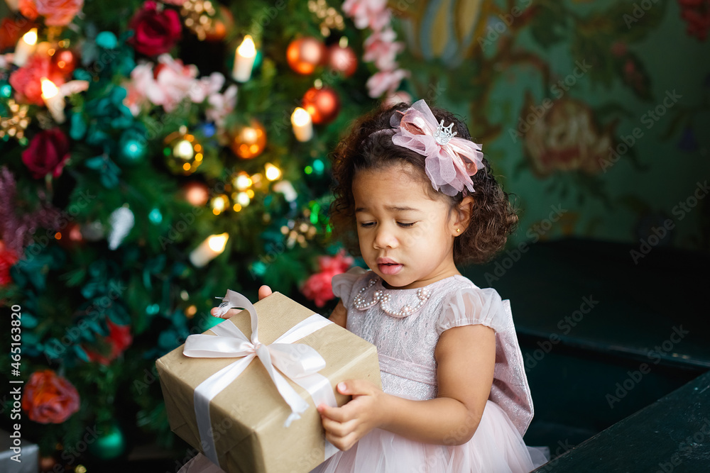 Cute African American little girl in pink dress with Christmas gift box or Christmas gift at home. Celebrating Christmas Holidays, Merry Christmas and Happy Holidays Cute African American little girl in pink dress with Christmas gift box or Christmas gift at home. Celebrating Christmas Holidays, Merry Christmas and Happy Holidays