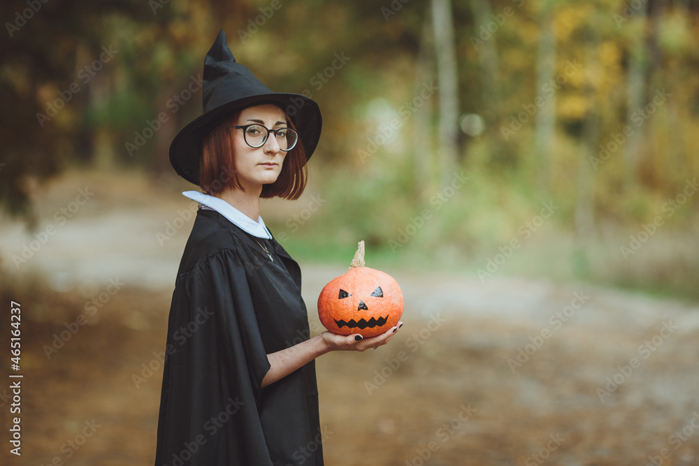 Halloween witch. Portrait of a girl in a hat and a witch costume with a pumpkin in the forest. Ready for the holiday